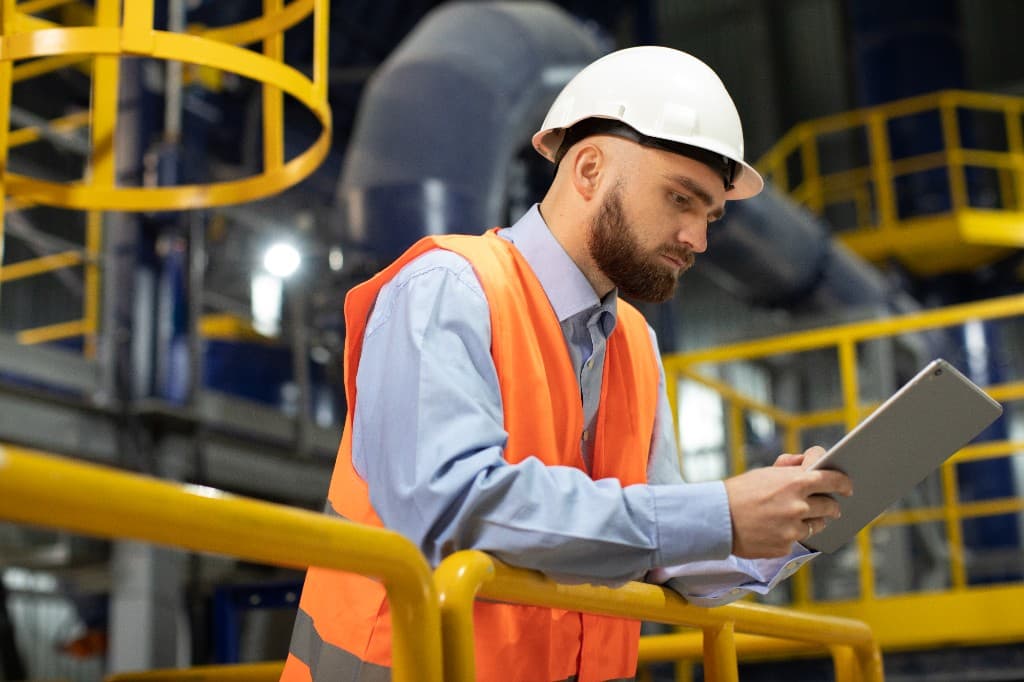 Engineer in safety gear reviewing work on a tablet at an industrial facility